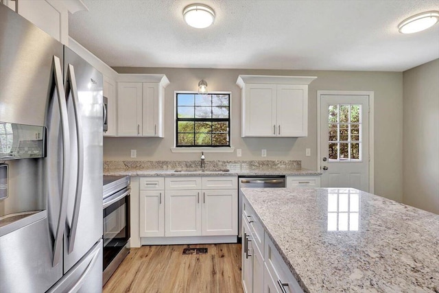 kitchen featuring appliances with stainless steel finishes, light hardwood / wood-style floors, white cabinets, light stone countertops, and sink