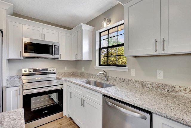 kitchen featuring appliances with stainless steel finishes, white cabinetry, light stone countertops, light hardwood / wood-style flooring, and sink