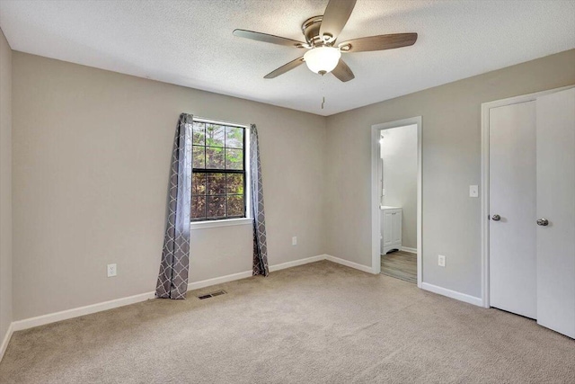 unfurnished bedroom with light carpet, ceiling fan, ensuite bathroom, and a textured ceiling