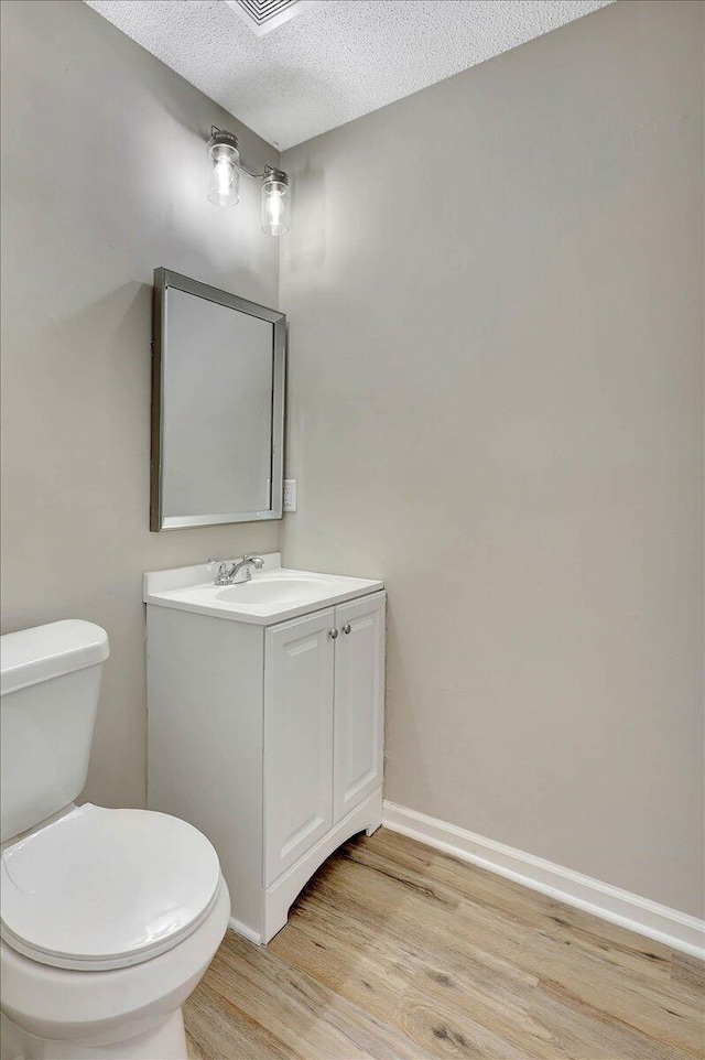 bathroom with a textured ceiling, hardwood / wood-style floors, vanity, and toilet