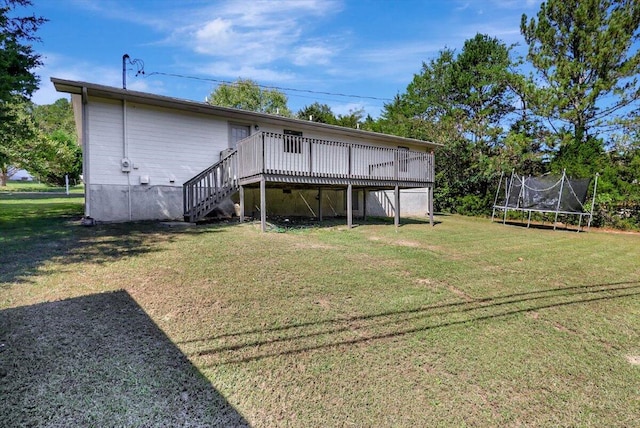 rear view of house with a wooden deck, a trampoline, and a lawn