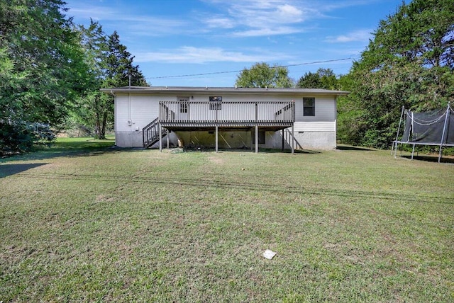 back of house with a trampoline, a wooden deck, and a lawn