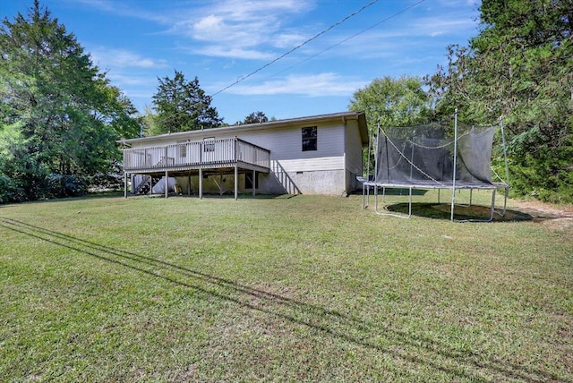 rear view of house with a trampoline, a wooden deck, and a lawn