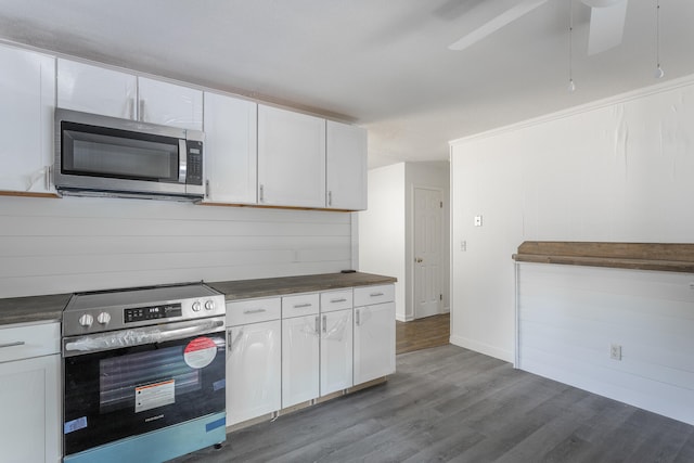 kitchen with stainless steel appliances, white cabinetry, hardwood / wood-style floors, and wooden walls