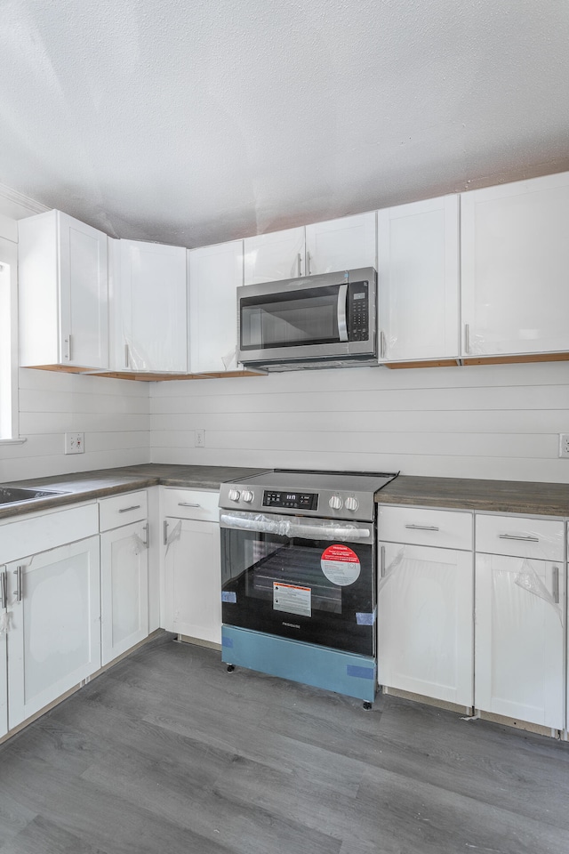 kitchen with appliances with stainless steel finishes, white cabinetry, and dark wood-type flooring