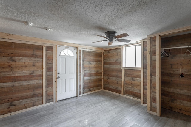 interior space featuring a textured ceiling, light hardwood / wood-style floors, wooden walls, and ceiling fan