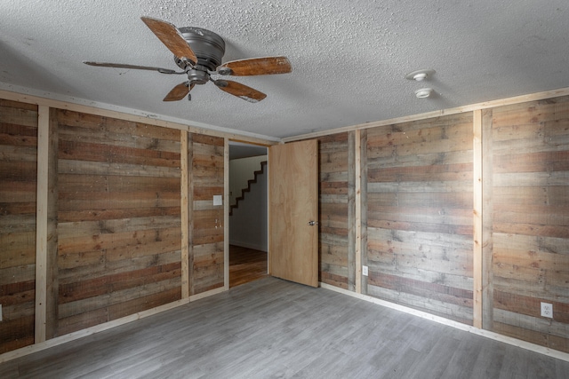 unfurnished room featuring wood walls, ceiling fan, hardwood / wood-style floors, and a textured ceiling