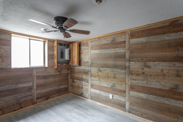 empty room featuring ceiling fan, electric panel, wood walls, a textured ceiling, and hardwood / wood-style flooring