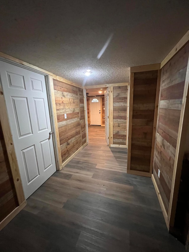 hall featuring a textured ceiling, wooden walls, and dark hardwood / wood-style flooring