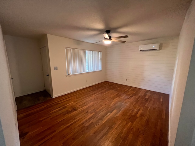 empty room featuring dark wood-type flooring, an AC wall unit, a textured ceiling, ceiling fan, and wooden walls