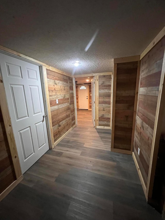 corridor with a textured ceiling, wooden walls, and dark wood-type flooring