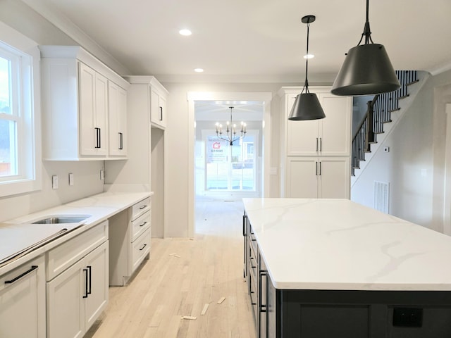 kitchen featuring decorative light fixtures, white cabinets, a center island, light stone counters, and light hardwood / wood-style flooring