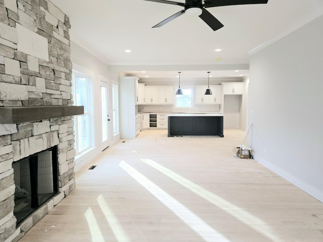 living room with crown molding, a fireplace, ceiling fan, and light wood-type flooring