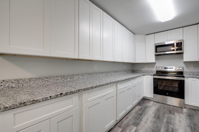 kitchen with light hardwood / wood-style floors, light stone countertops, stainless steel appliances, and white cabinets