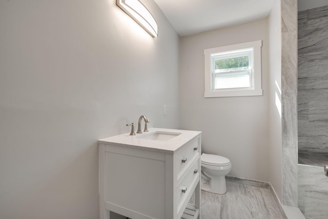 bathroom with a tile shower, vanity, and toilet