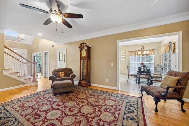 living area with ornamental molding, light wood-type flooring, and ceiling fan with notable chandelier