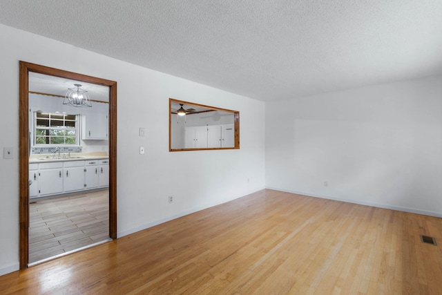 spare room featuring light wood-type flooring, a chandelier, sink, and a textured ceiling