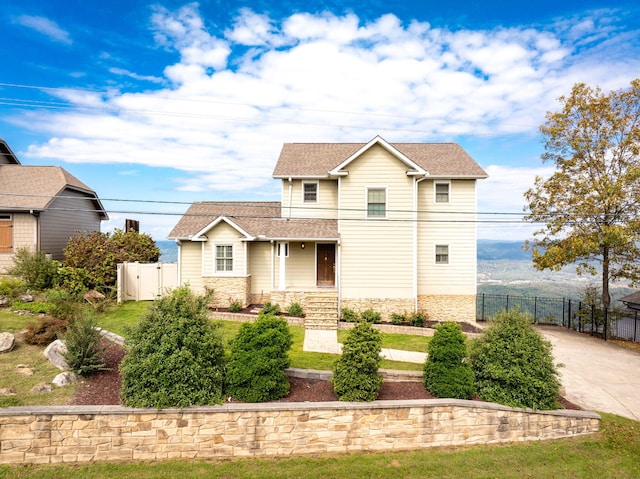 view of front of house featuring stone siding, a shingled roof, fence, and a gate