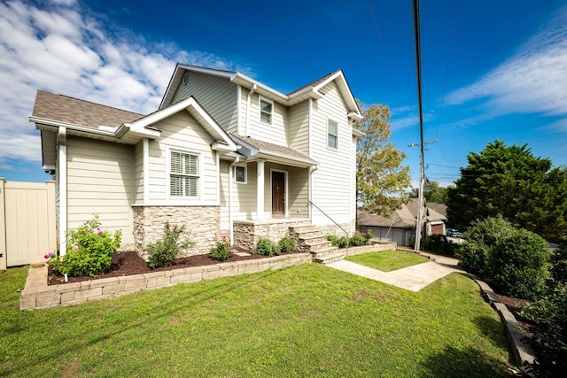 view of front of property with stone siding, a front lawn, a shingled roof, and fence