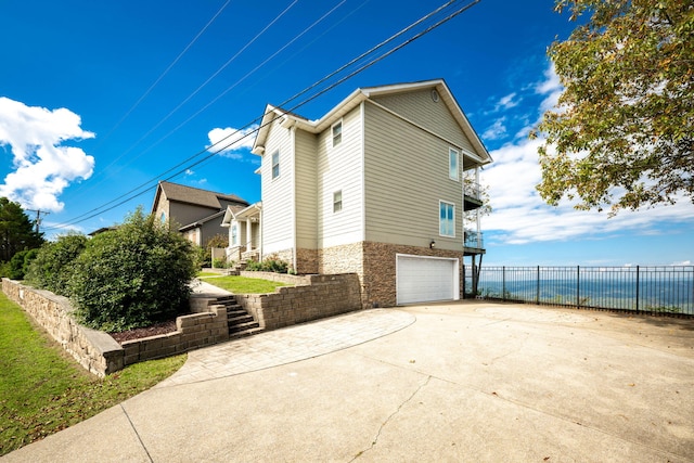 view of side of home with an attached garage, driveway, a water view, and fence