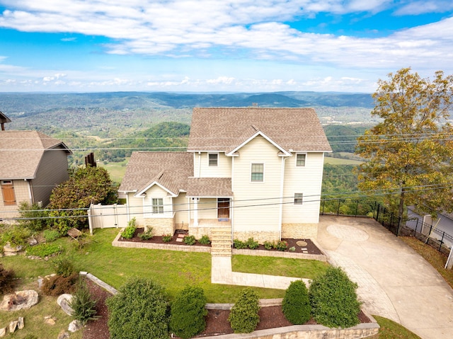 view of front of property with concrete driveway, roof with shingles, fence, a mountain view, and a front yard