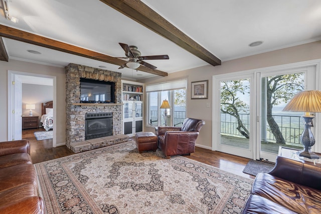 living room featuring baseboards, ornamental molding, wood finished floors, beamed ceiling, and a stone fireplace