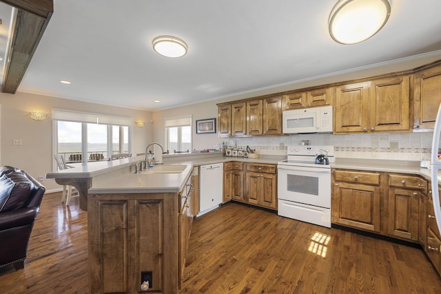 kitchen with brown cabinetry, dark wood-type flooring, a sink, white appliances, and a peninsula