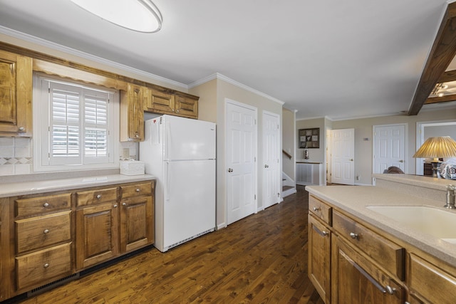 kitchen with brown cabinets, dark wood finished floors, light countertops, freestanding refrigerator, and a sink