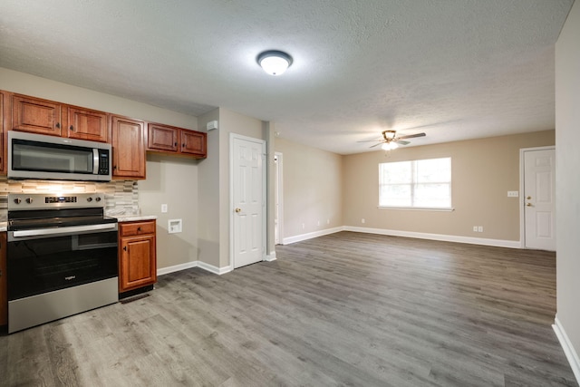 kitchen featuring appliances with stainless steel finishes, decorative backsplash, a textured ceiling, light wood-type flooring, and ceiling fan