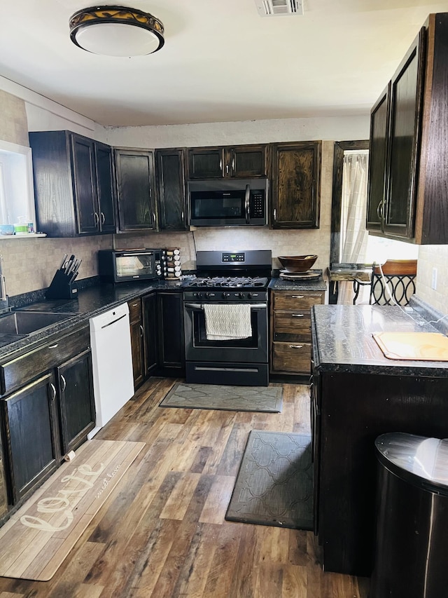 kitchen featuring dark countertops, gas range oven, tasteful backsplash, a sink, and dishwasher