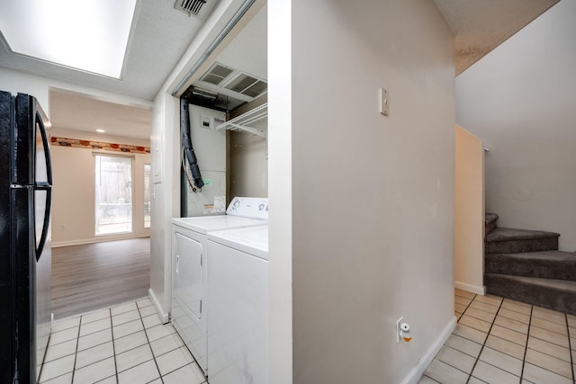 clothes washing area featuring a textured ceiling, washing machine and clothes dryer, and light tile patterned floors