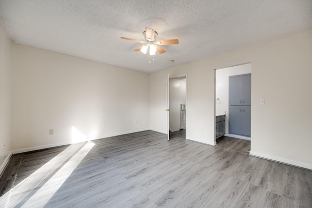 unfurnished bedroom with connected bathroom, a textured ceiling, light wood-type flooring, and ceiling fan