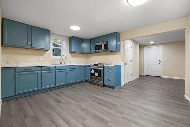 kitchen featuring blue cabinets, sink, a textured ceiling, stainless steel appliances, and light wood-type flooring