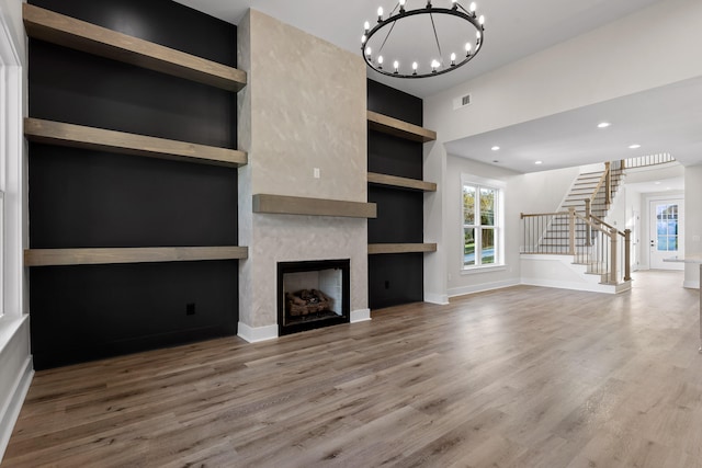 unfurnished living room featuring hardwood / wood-style floors, a notable chandelier, a fireplace, and built in shelves