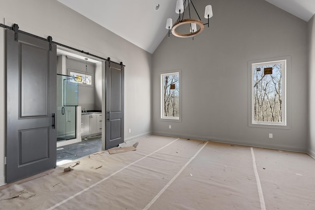 unfurnished bedroom with high vaulted ceiling, a barn door, multiple windows, and baseboards