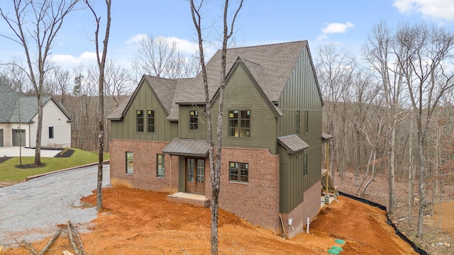 view of front facade with brick siding, board and batten siding, driveway, and a shingled roof