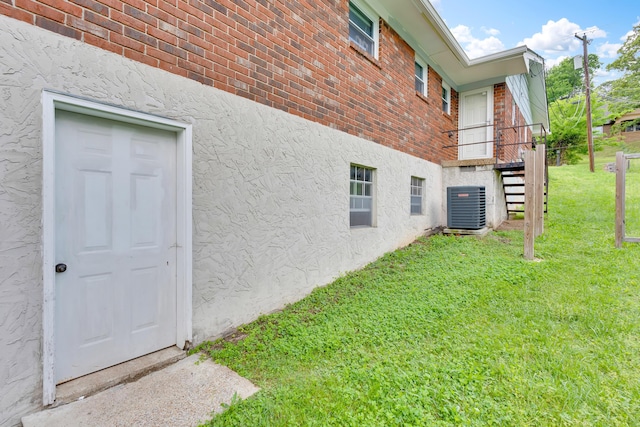 view of side of property featuring central air condition unit, a lawn, brick siding, and stucco siding