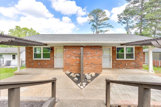 back of property with brick siding, a pergola, a patio area, and roof with shingles