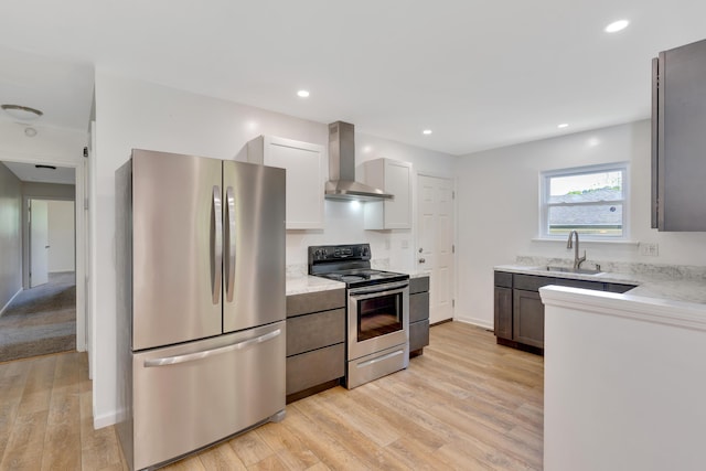 kitchen with wall chimney range hood, light stone countertops, a sink, light wood-style floors, and stainless steel appliances