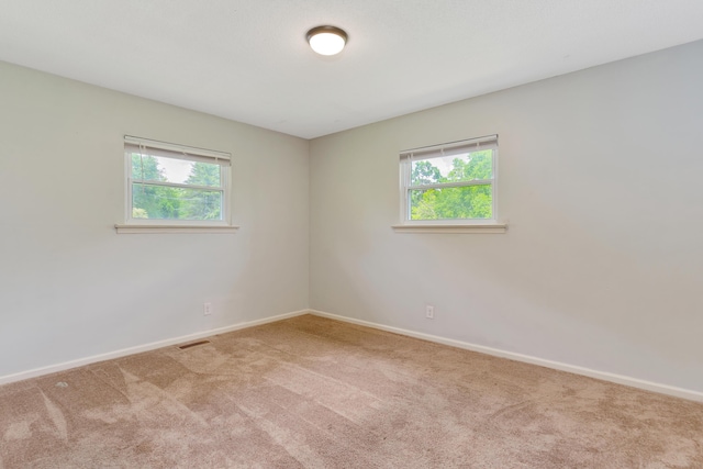 empty room with carpet floors, baseboards, a healthy amount of sunlight, and visible vents
