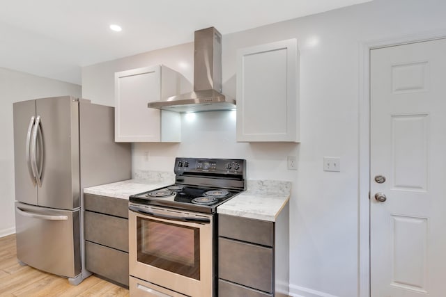 kitchen featuring light stone countertops, light wood-style floors, wall chimney exhaust hood, stainless steel appliances, and white cabinetry