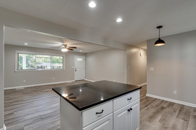 kitchen with a kitchen island, ceiling fan, hanging light fixtures, white cabinetry, and light hardwood / wood-style flooring