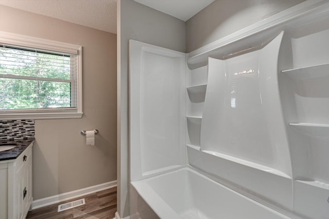 bathroom with vanity, hardwood / wood-style floors, washtub / shower combination, and decorative backsplash