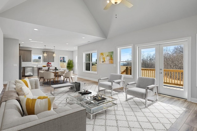 living room with ceiling fan, high vaulted ceiling, light wood-type flooring, and a wealth of natural light