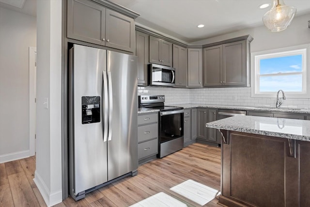 kitchen featuring decorative backsplash, light wood-type flooring, stainless steel appliances, sink, and light stone counters