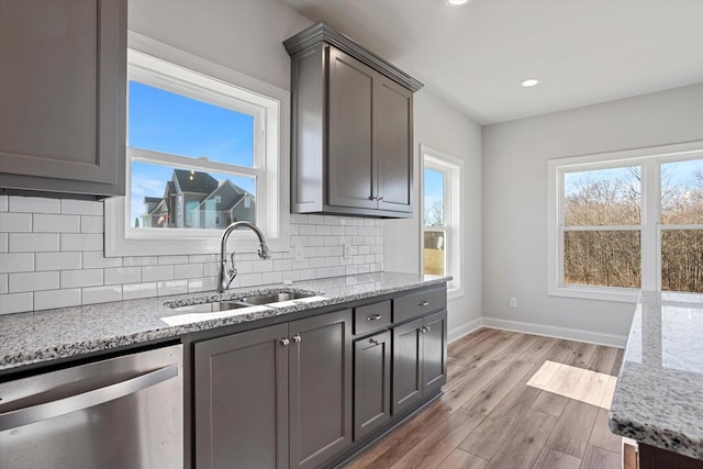 kitchen with sink, dishwasher, light stone counters, and light wood-type flooring