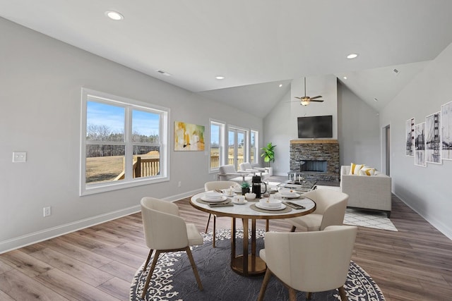 dining room featuring ceiling fan, a stone fireplace, high vaulted ceiling, and light wood-type flooring