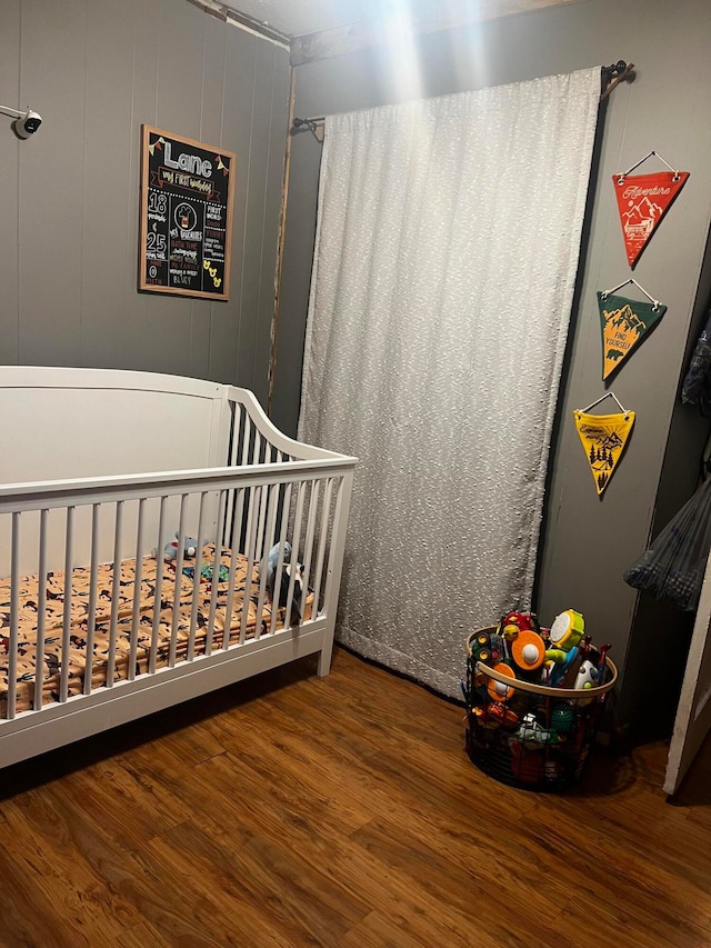 bedroom with a crib, hardwood / wood-style flooring, and wooden walls