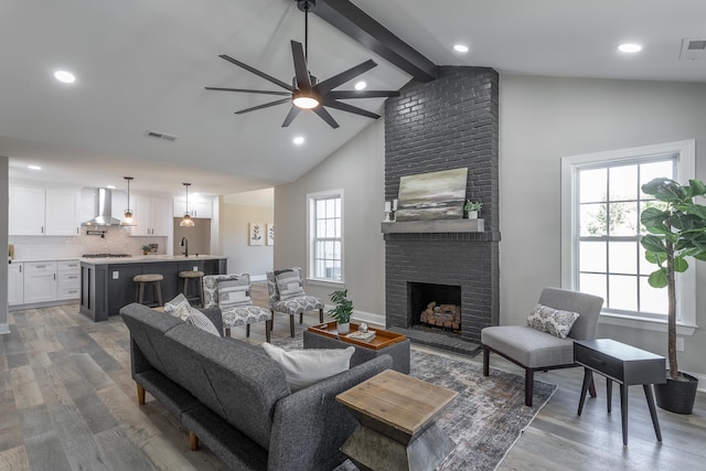 living room featuring high vaulted ceiling, ceiling fan, hardwood / wood-style flooring, a fireplace, and beam ceiling