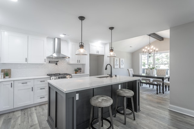 kitchen featuring wall chimney range hood, a kitchen island with sink, sink, and white cabinets